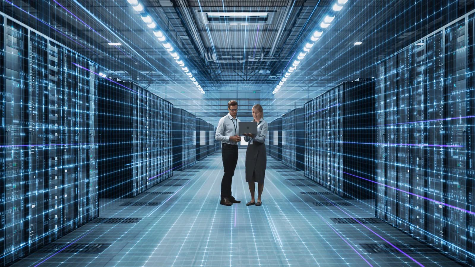 Two engineers reviewing a laptop in a data-centre aisle lit by network traffic