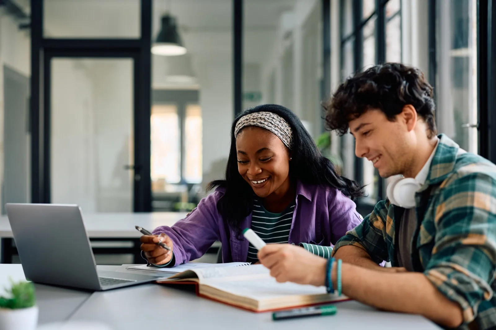 Two students smile while studying together at a laptop with an open textbook