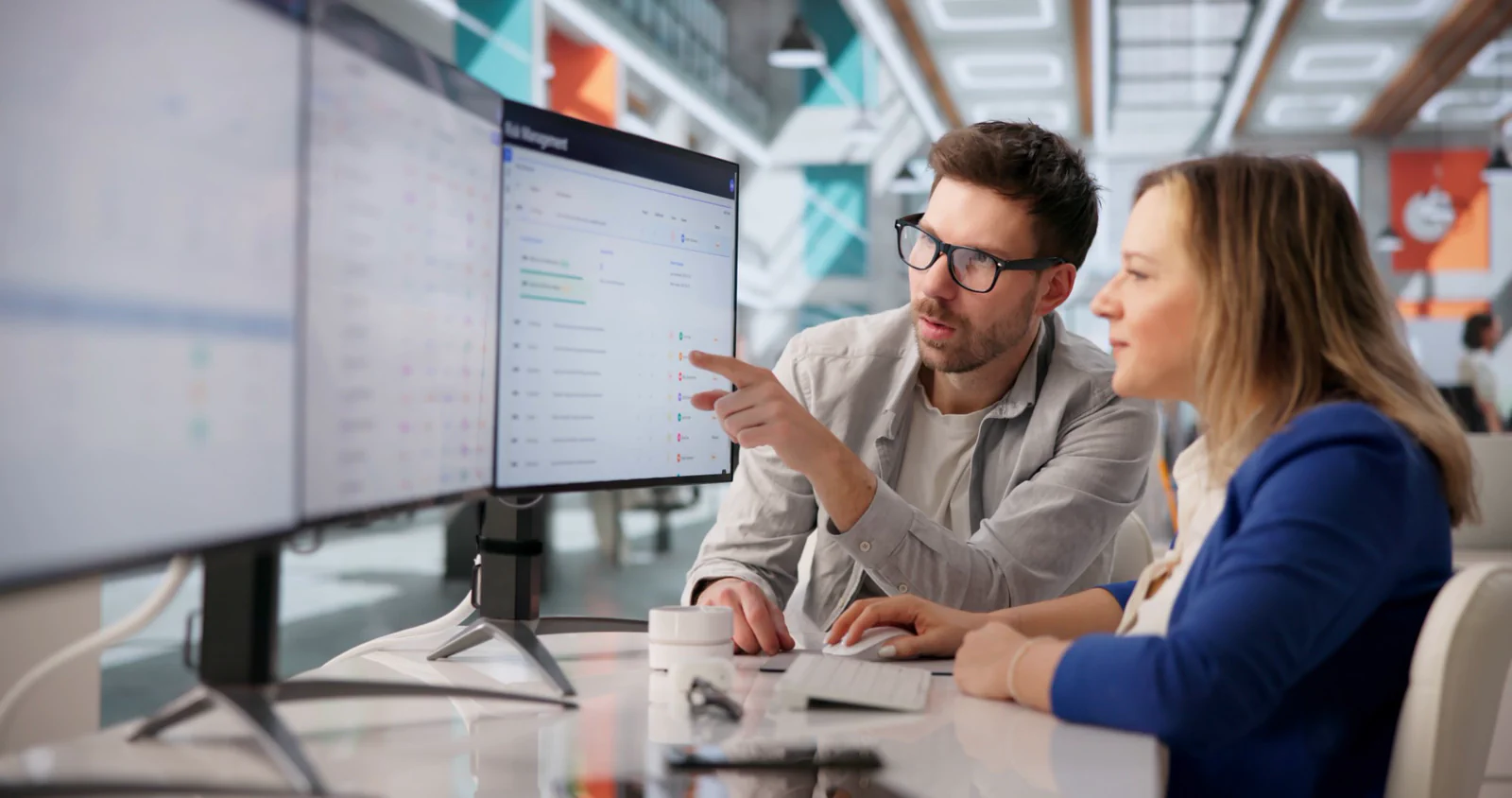 Two colleagues reviewing a dashboard together on a large monitor